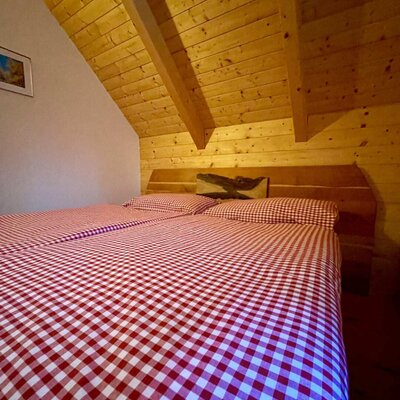 Double bed with red and white checkered bedding in an Alm bedroom with wooden ceilings and sloped walls.