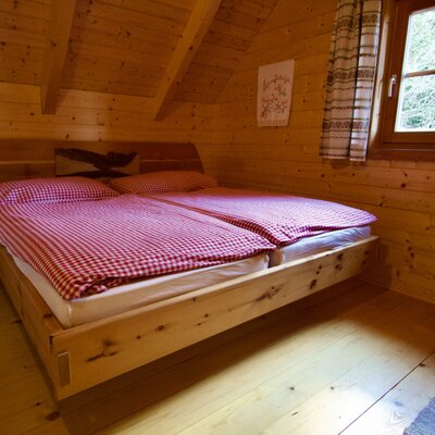 Bedroom in the Alm with a wooden bed, red and white checkered bedding, and a window.