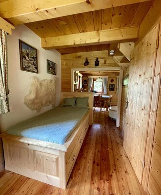 A cozy sleeping area in the Alm featuring a rustic wooden bed and warm timber wall paneling.