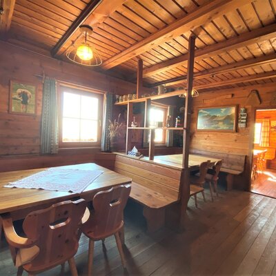 The dining area in the Alpine Hut features wooden tables, benches, and chairs, with a window providing natural light.