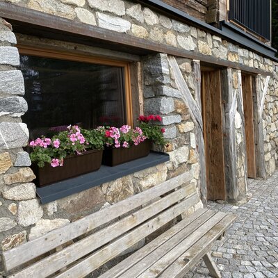 An inviting seating area outside the Alm with a rustic wooden bench and vibrant flower boxes on the windowsill.