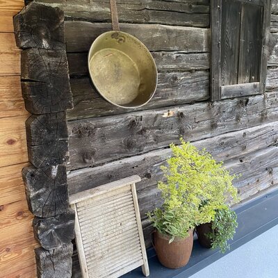 Charmingly decorated wooden exterior of the alm, featuring rustic details like an old brass pan, a vintage washboard, and green potted plants.