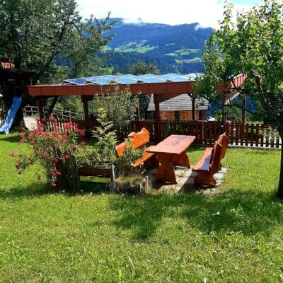 Outdoor seating area in the farm house garden with a wooden picnic table, mountain views, a children's slide, and a nearby structure featuring solar panels.