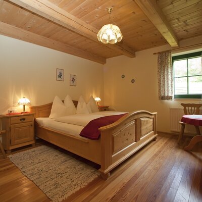 Double bedroom in the farmhouse, featuring a wooden bed, two nightstands, a wardrobe, and a beamed wooden ceiling.