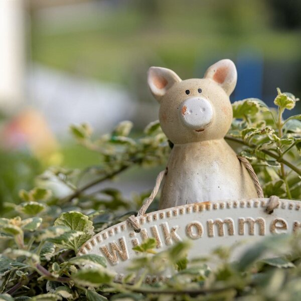 A pig figurine holding a 'Willkommen' (Welcome) sign among green foliage, a welcoming detail at the Farm House.