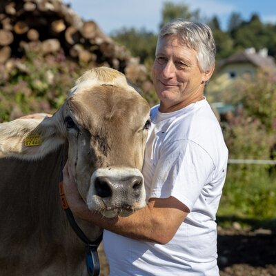 A man with a brown cow, part of the farm animals present at the farm house.