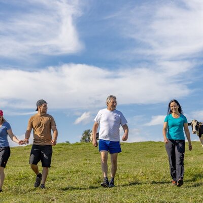 A group of people walking in a grassy field alongside a cow at the Farm House.
