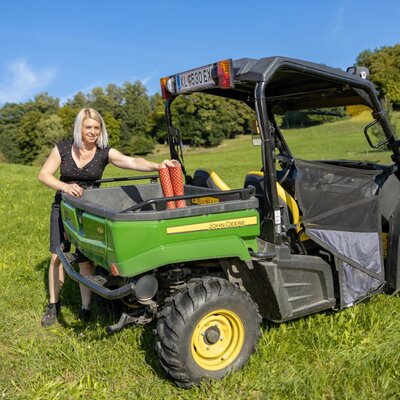 A John Deere utility vehicle with red rain boots in the cargo bed, parked on the farm house grounds.