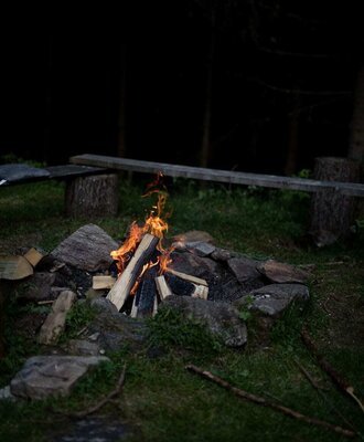 Campfire area at the Alm with burning wood and a wooden bench in the background.