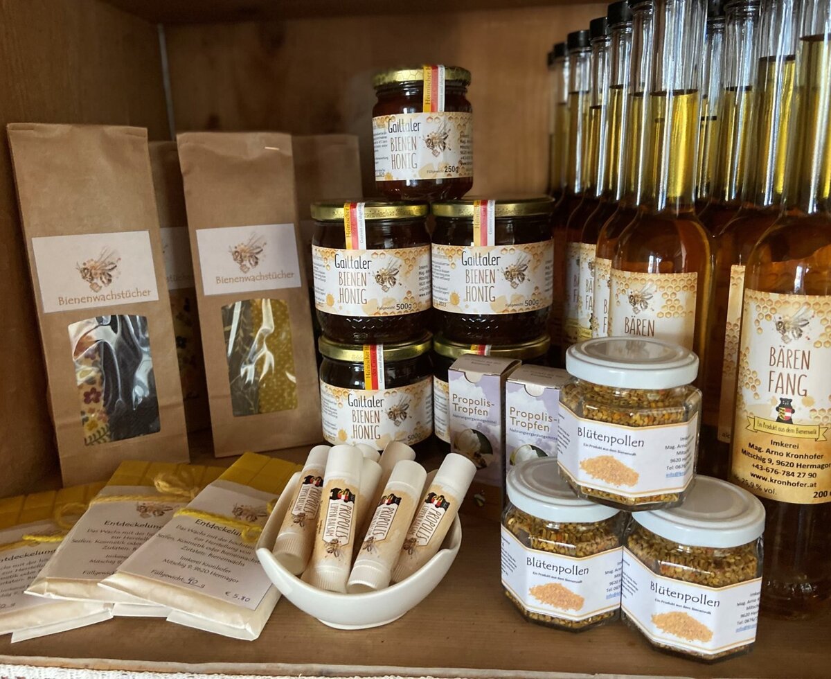 A display of local bee products from the Farm House, including honey, propolis items, pollen, beeswax wraps, and bottled beverages.