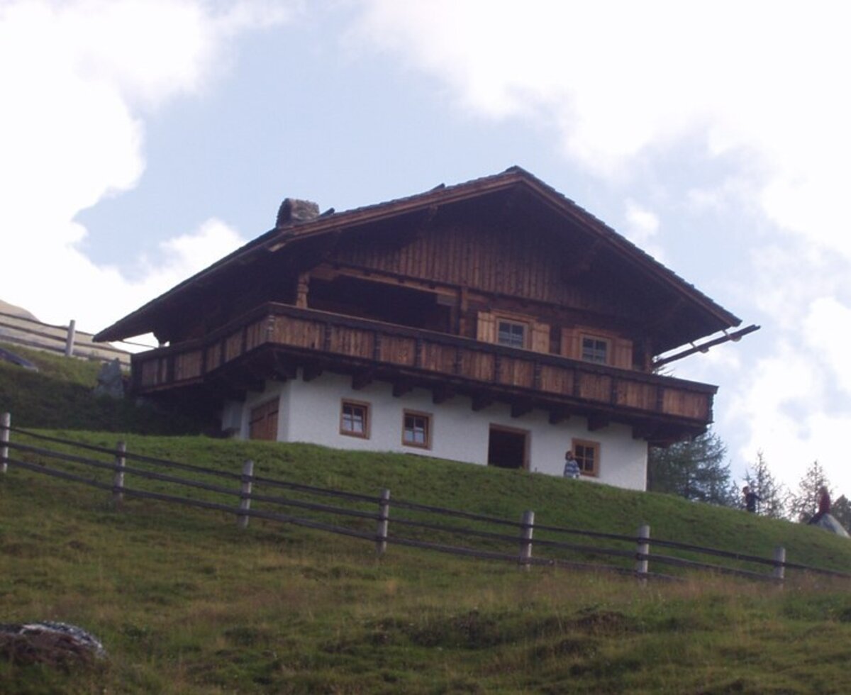 An inviting, rustic Alm nestled on a grassy hillside with a traditional wooden balcony.