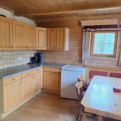 The alm's cozy kitchen featuring wooden cabinetry, a bright dining area, and a window offering green views.