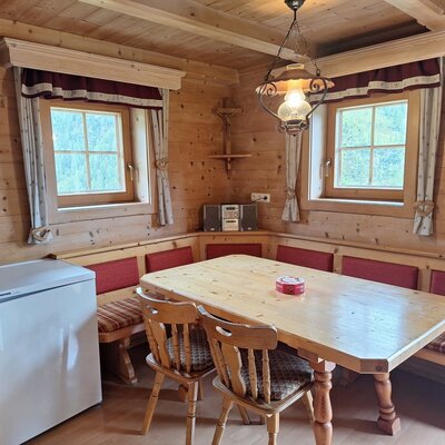 The Alm's cozy dining area featuring a traditional wooden corner bench, a large dining table, and warm lighting.