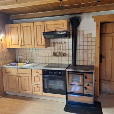 The Alm's cozy kitchen featuring rustic wooden cabinetry, a modern stove, and a traditional wood-burning oven.