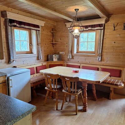 A cozy dining area in the Alm featuring a rustic wooden corner bench, a large table, and warm wood-paneled walls.