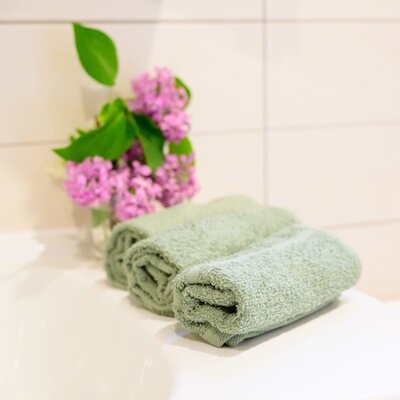 Rolled green towels and a vase of lilac flowers are placed on the sink in the farm house bathroom.