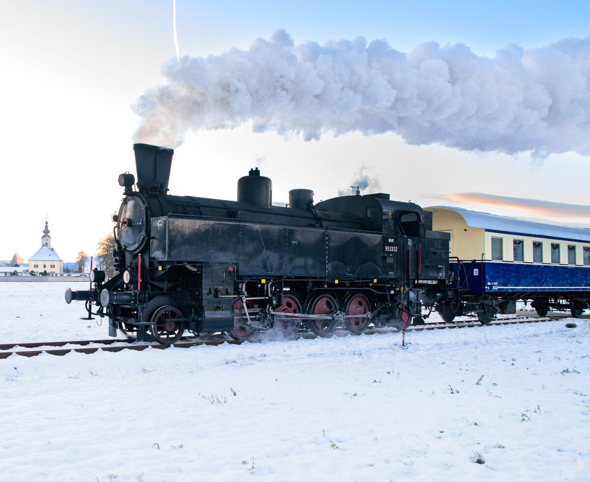 A historic steam train, featuring a black locomotive and blue passenger car, travels through the snowy landscape, a nearby attraction for guests of the Farm House.