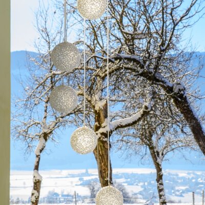 View from the farmhouse window of a snowy winter landscape with trees and decorative balls in the foreground.