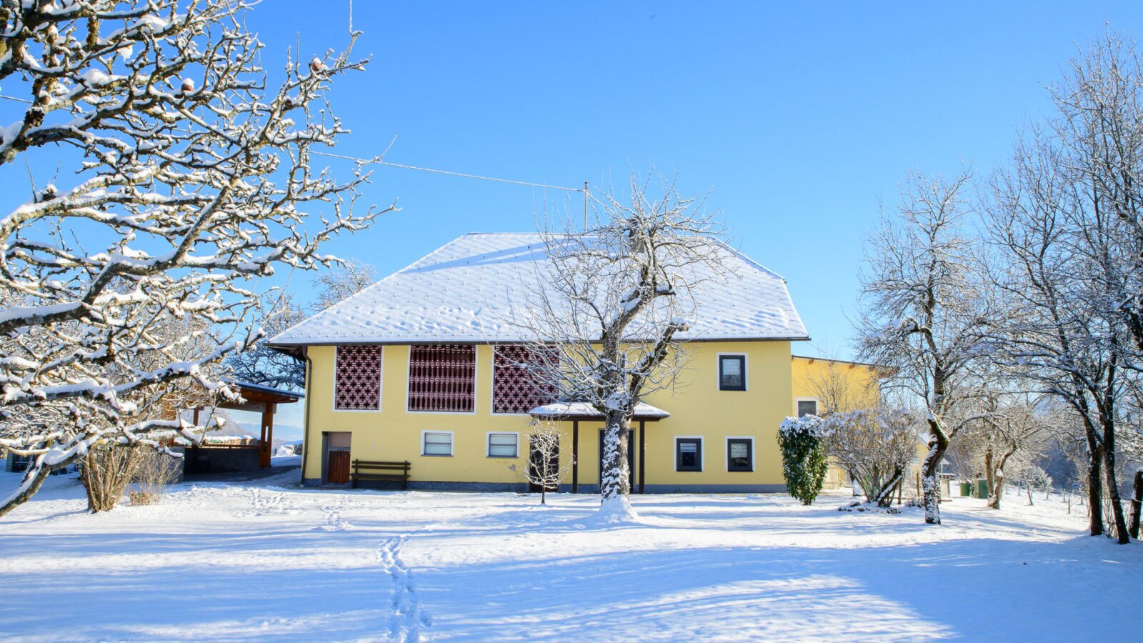 Exterior view of the yellow farmhouse with a snow-covered roof and winter landscape under a blue sky.