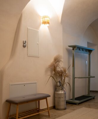 The entrance hallway of the farm house features arched ceilings, a bench with shoe storage, and a wooden coat stand.