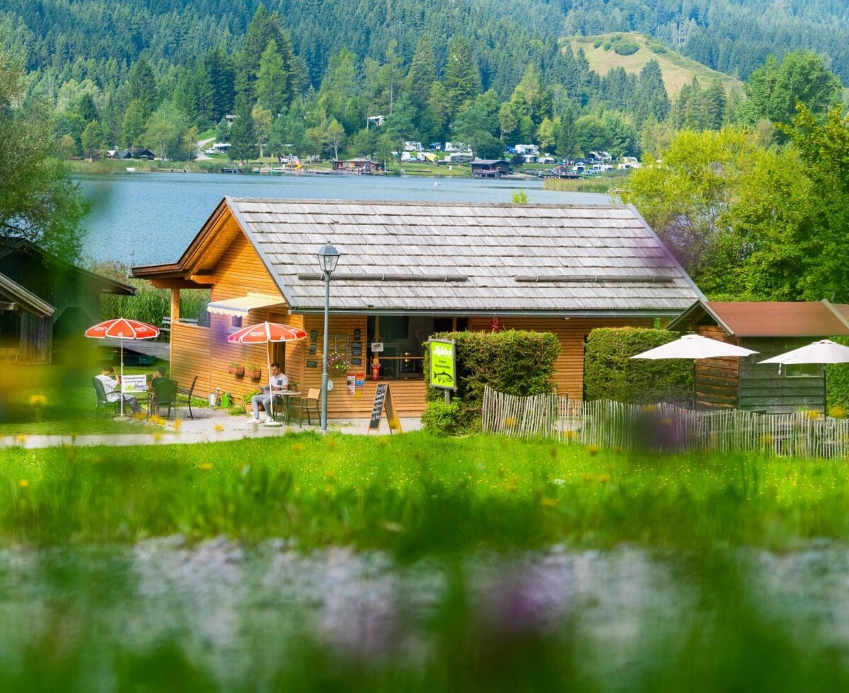 The farmhouse's wooden building with an outdoor terrace, seating, and a view of Lake Weissensee.