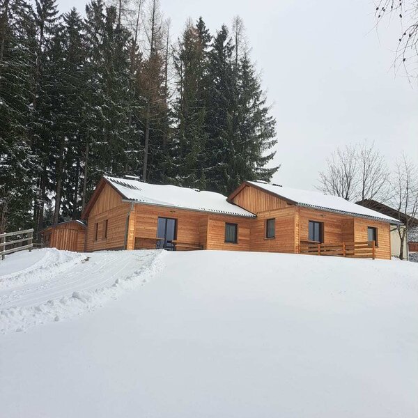 The Alm building with a wooden facade in a snowy landscape, surrounded by pine trees.