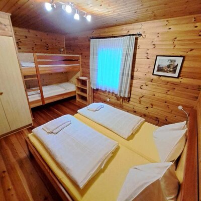 Bedroom of the Alm with two single beds, a bunk bed, and wooden walls.