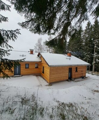 Exterior view of the Alm with a wooden facade, snow-covered roof, and surrounding trees.