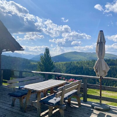 The Alpine Hut features a wooden dining set with benches and cushions on a terrace, offering panoramic mountain views.