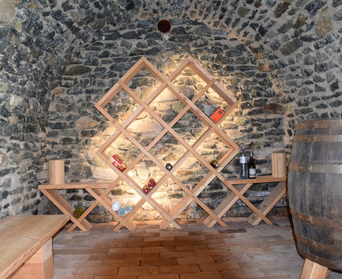 The Alpine Hut's stone-walled wine cellar features a vaulted ceiling, wooden wine rack, large barrel, and bench seating.