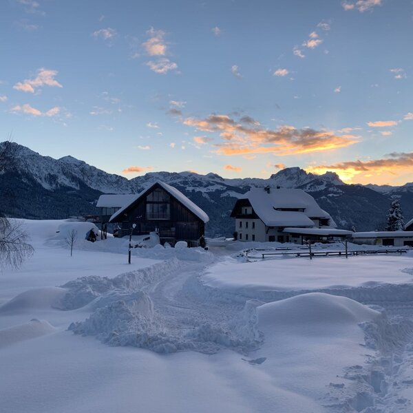 The Farm House buildings stand in a snow-covered landscape with the Karnisch Alps visible under a sunset sky.