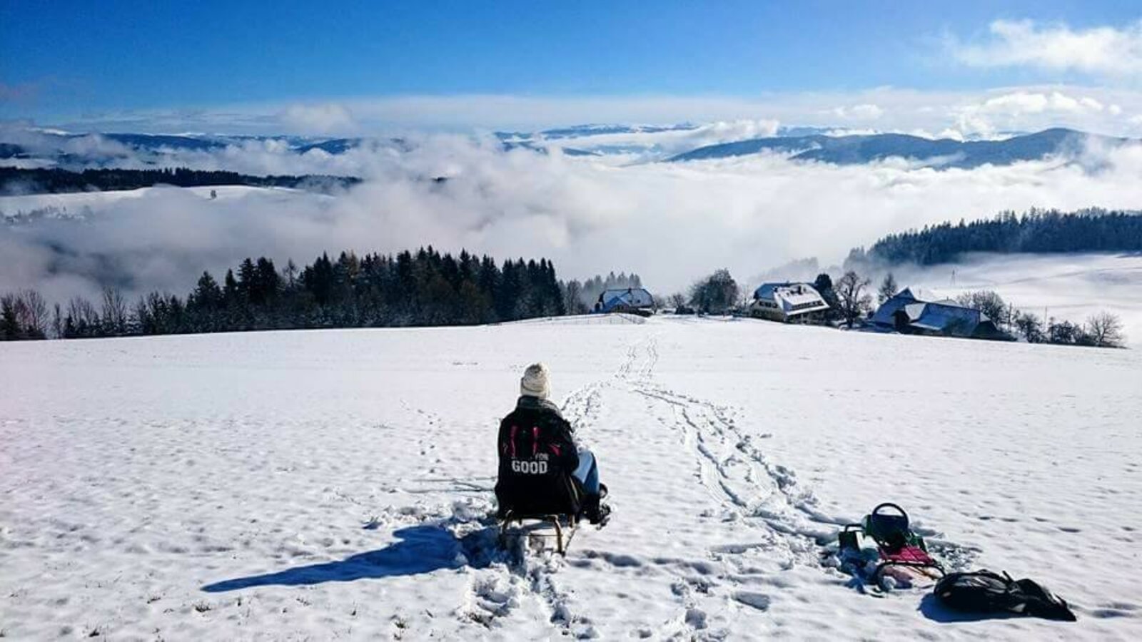 A person sledding in a snowy field at the Farm House, with views over clouds and distant mountains.