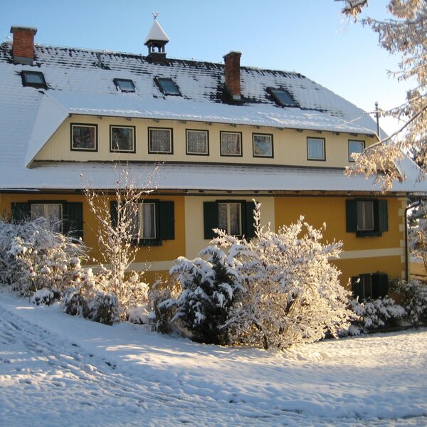The farmhouse exterior with a yellow facade and green shutters, covered in snow in winter.