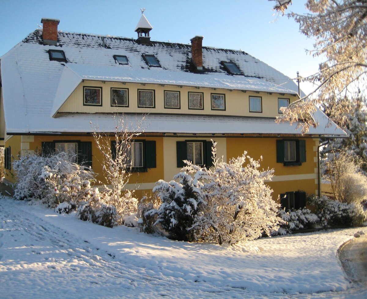 The farmhouse exterior with a yellow facade and green shutters, covered in snow in winter.
