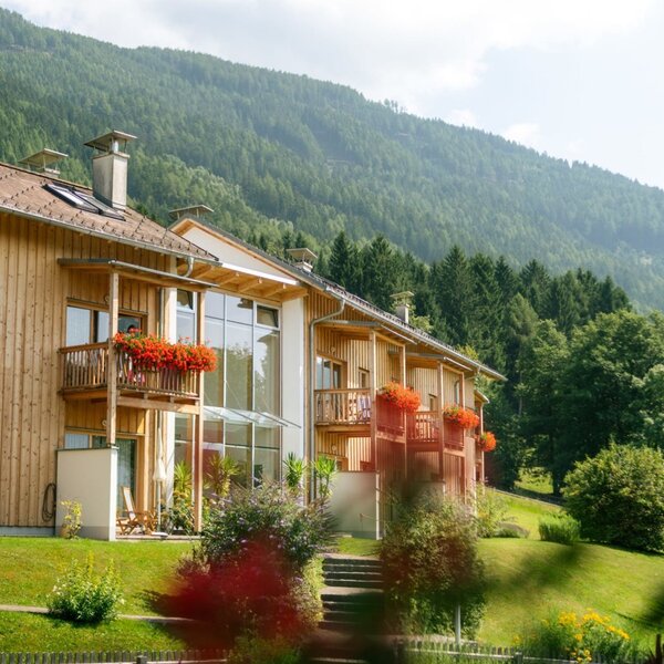 Exterior view of the farmhouse apartments, featuring wooden construction, balconies with flowers, and mountain views.