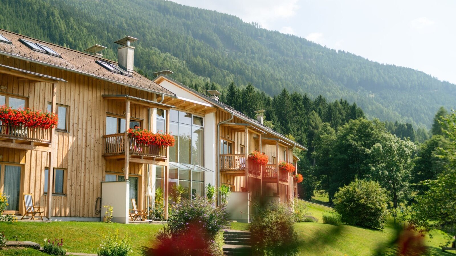 Exterior view of the farmhouse apartments, featuring wooden construction, balconies with flowers, and mountain views.