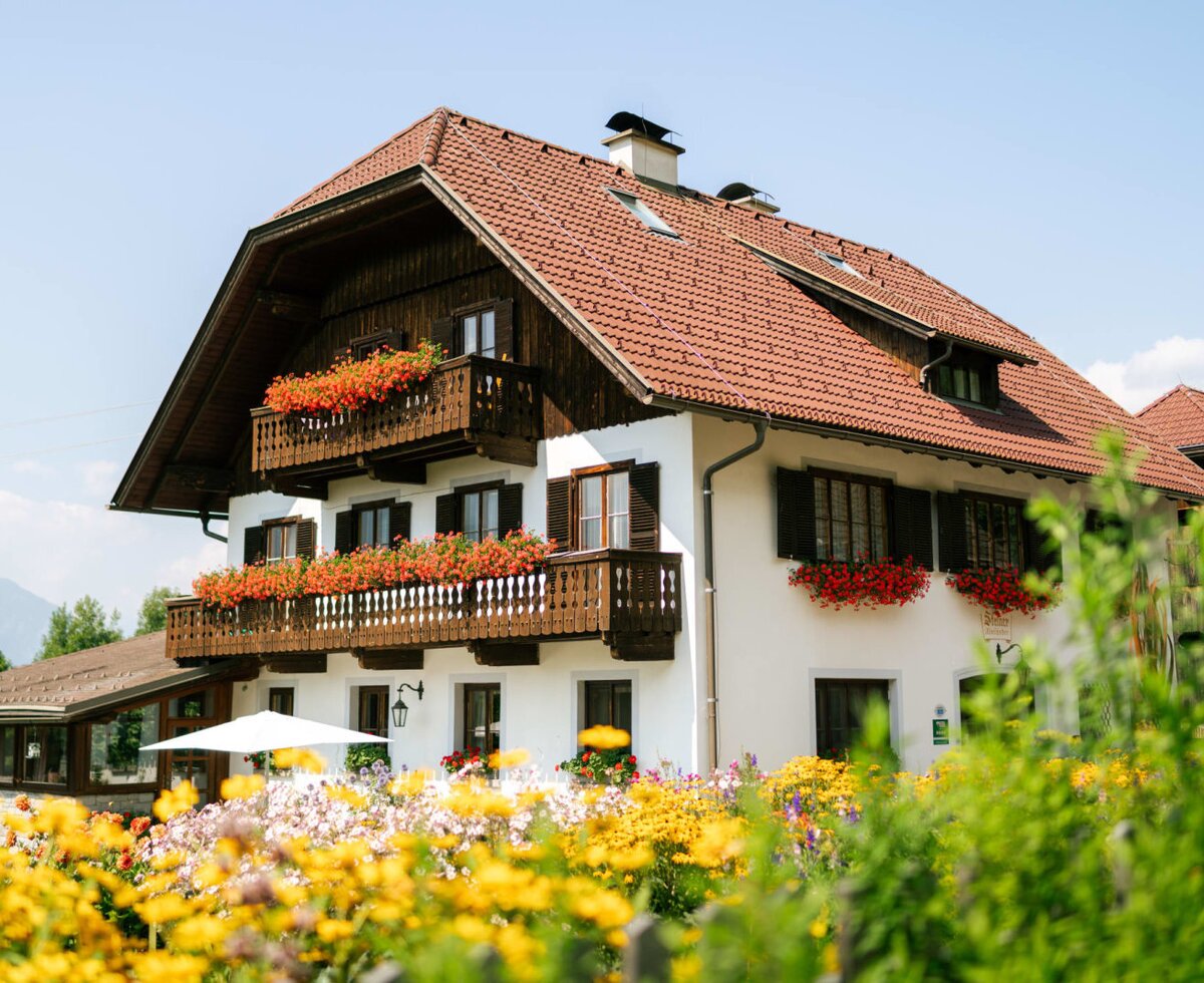 Exterior of the farmhouse featuring flower-adorned balconies, a colorful garden, and mountain views.