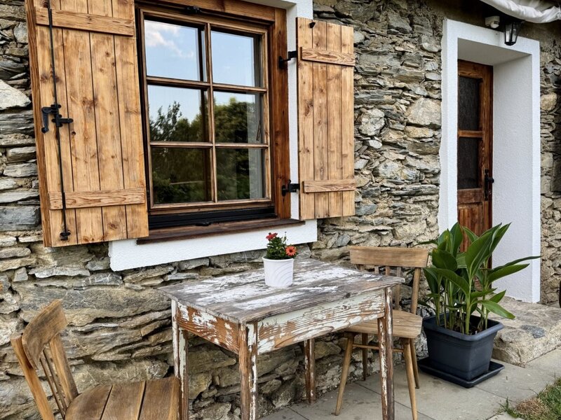 Exterior of the farmhouse with a stone facade, wooden shutters, and outdoor seating.