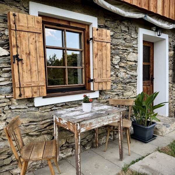 Exterior of the farmhouse with a stone facade, wooden shutters, and outdoor seating.