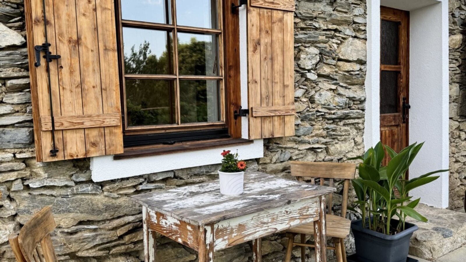 Exterior of the farmhouse with a stone facade, wooden shutters, and outdoor seating.