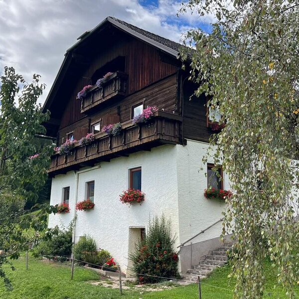 The inviting farmhouse featuring flower-decked wooden balconies and a spacious green garden.