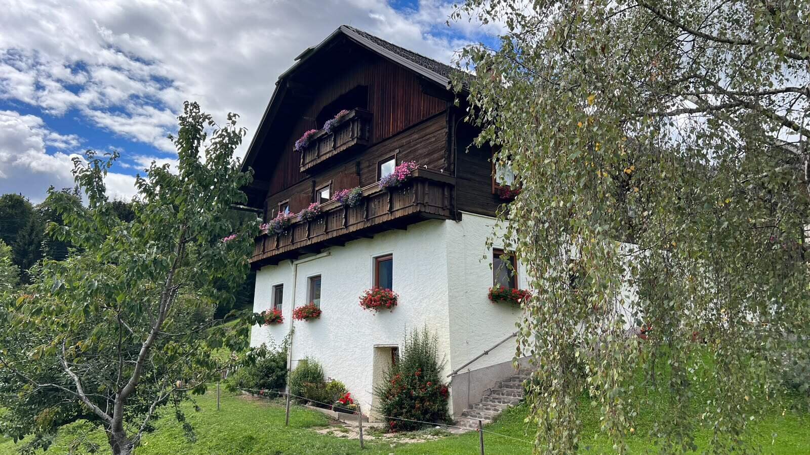 The inviting farmhouse featuring flower-decked wooden balconies and a spacious green garden.