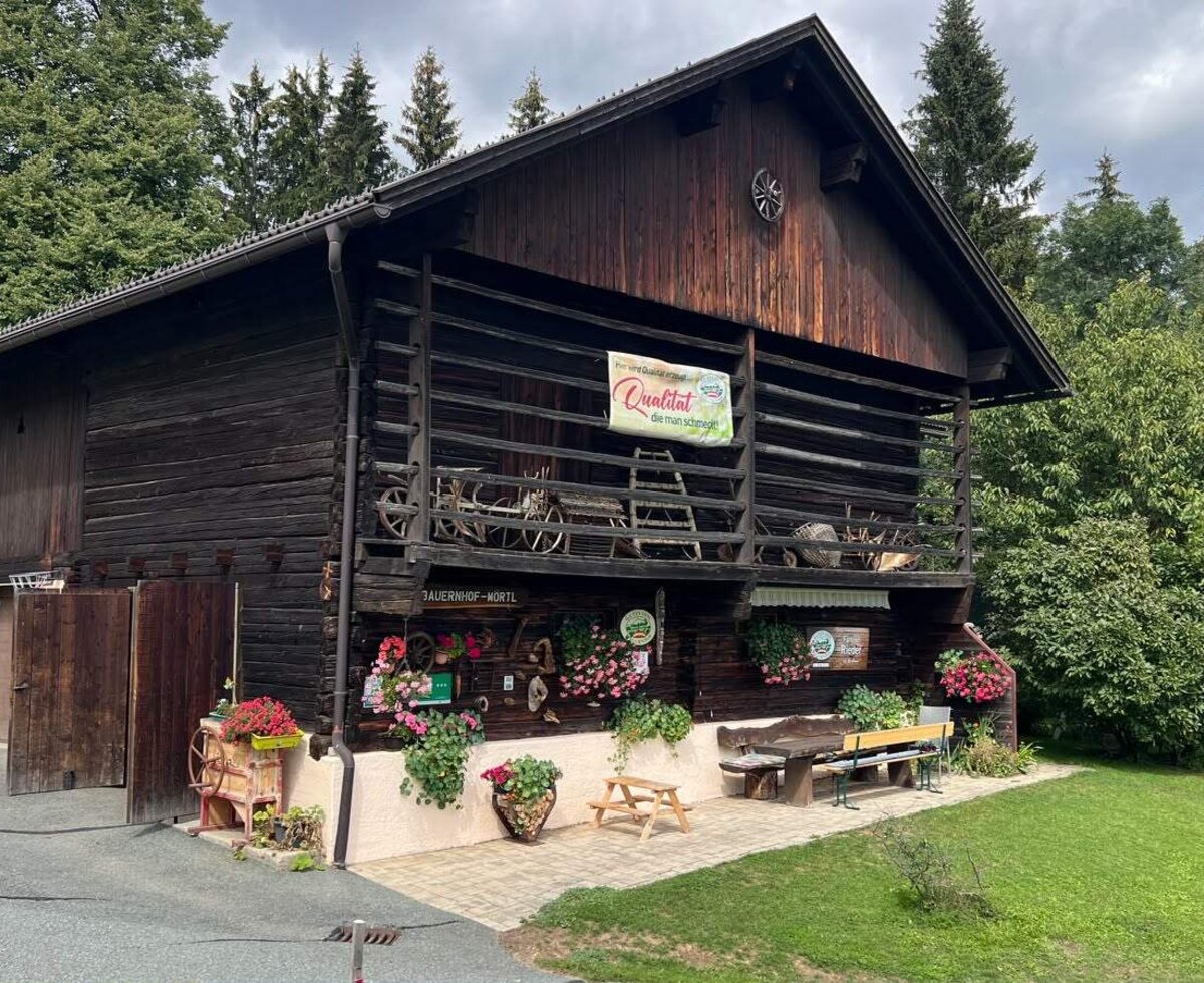 The farmhouse's rustic wooden barn featuring inviting outdoor seating, colorful potted flowers, and a lush green lawn.