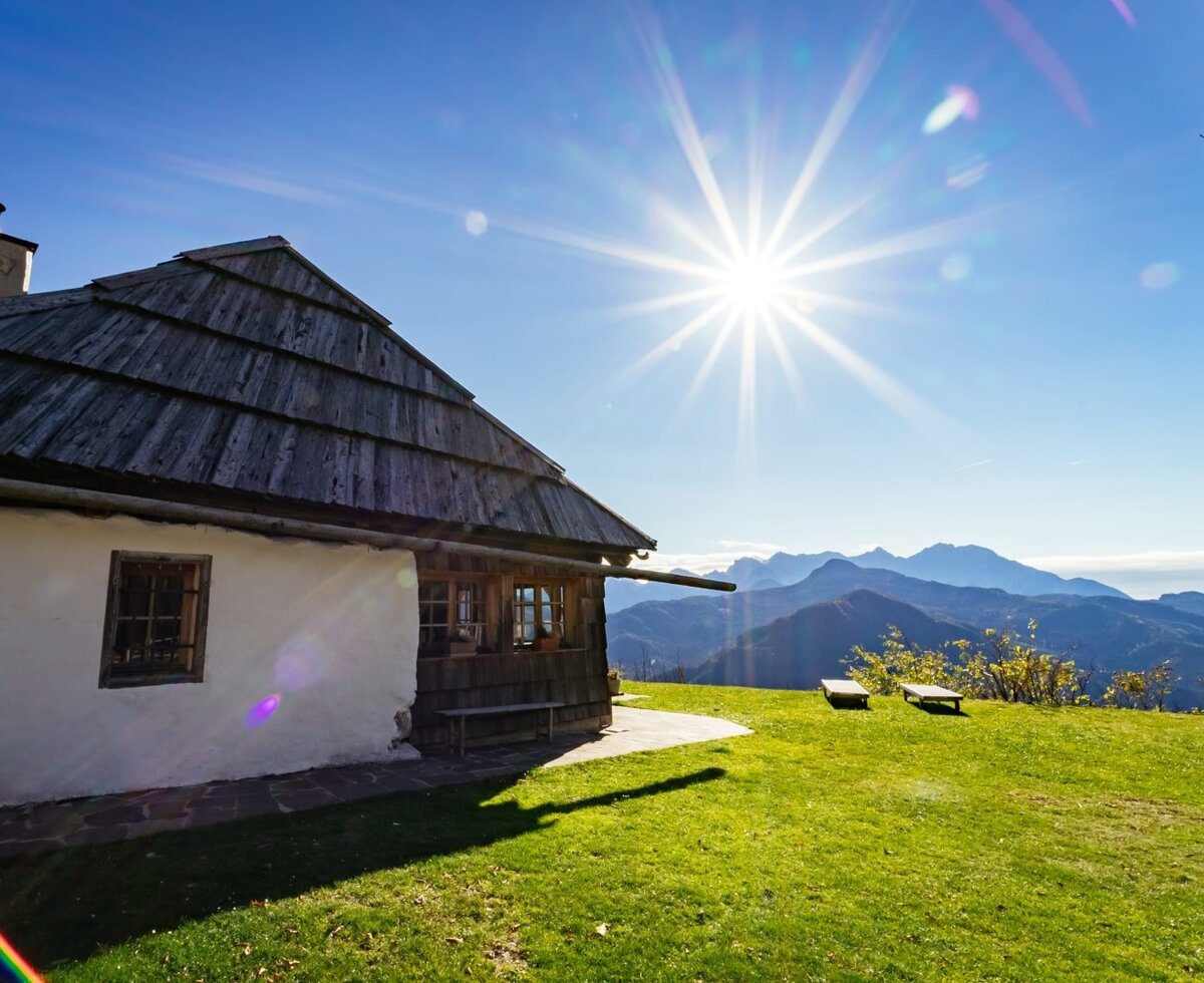 The farmhouse exterior, featuring a wooden shingle roof, white walls, a green lawn with benches, and distant mountain views.