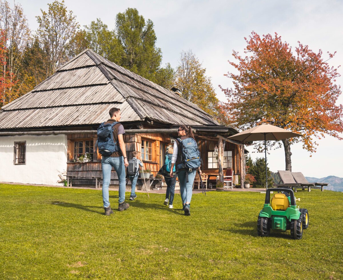 The traditional farmhouse exterior, set on a grassy lawn with outdoor seating, includes a child's ride-on toy and offers views of the surrounding mountains.