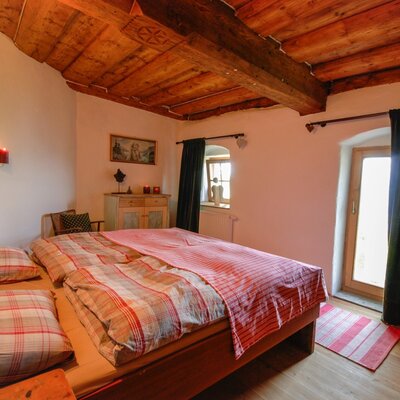 The double bedroom in the farmhouse features exposed wooden ceiling beams, a wooden bed, a wardrobe, and a door offering outdoor access.