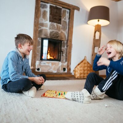 Children playing a board game on the rug in front of the lit fireplace in the Alpine Hut.