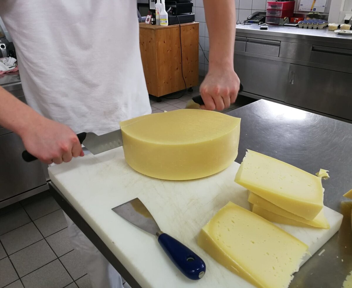 A staff member cuts a large wheel of cheese in the farmhouse kitchen, ready for guests.