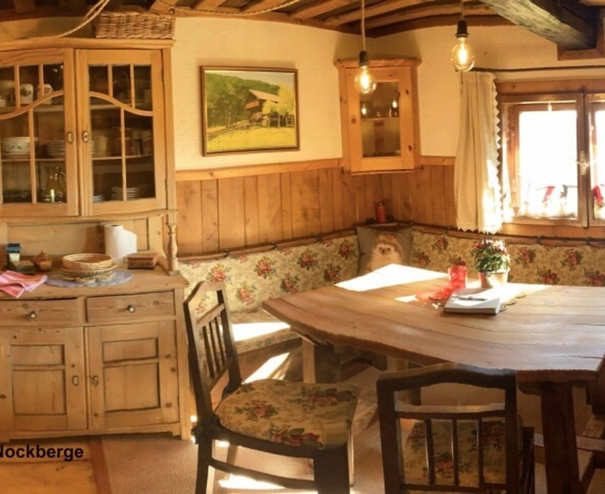 The Bauernstube of the Almhütte, featuring a wood stove, a fully equipped kitchen, a corner bench, a dining table, and grand-grand mothers wedding-bed