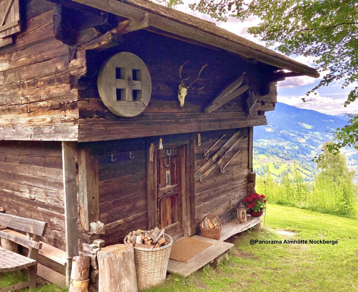 The rustic wooden exterior of the Almhütte, featuring traditional decorations and a panoramic view of the mountains and valley.